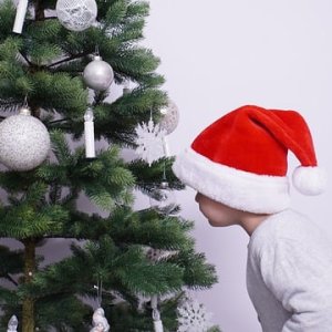Enfant avec chapeau de noel devant un sapin décoré en blanc